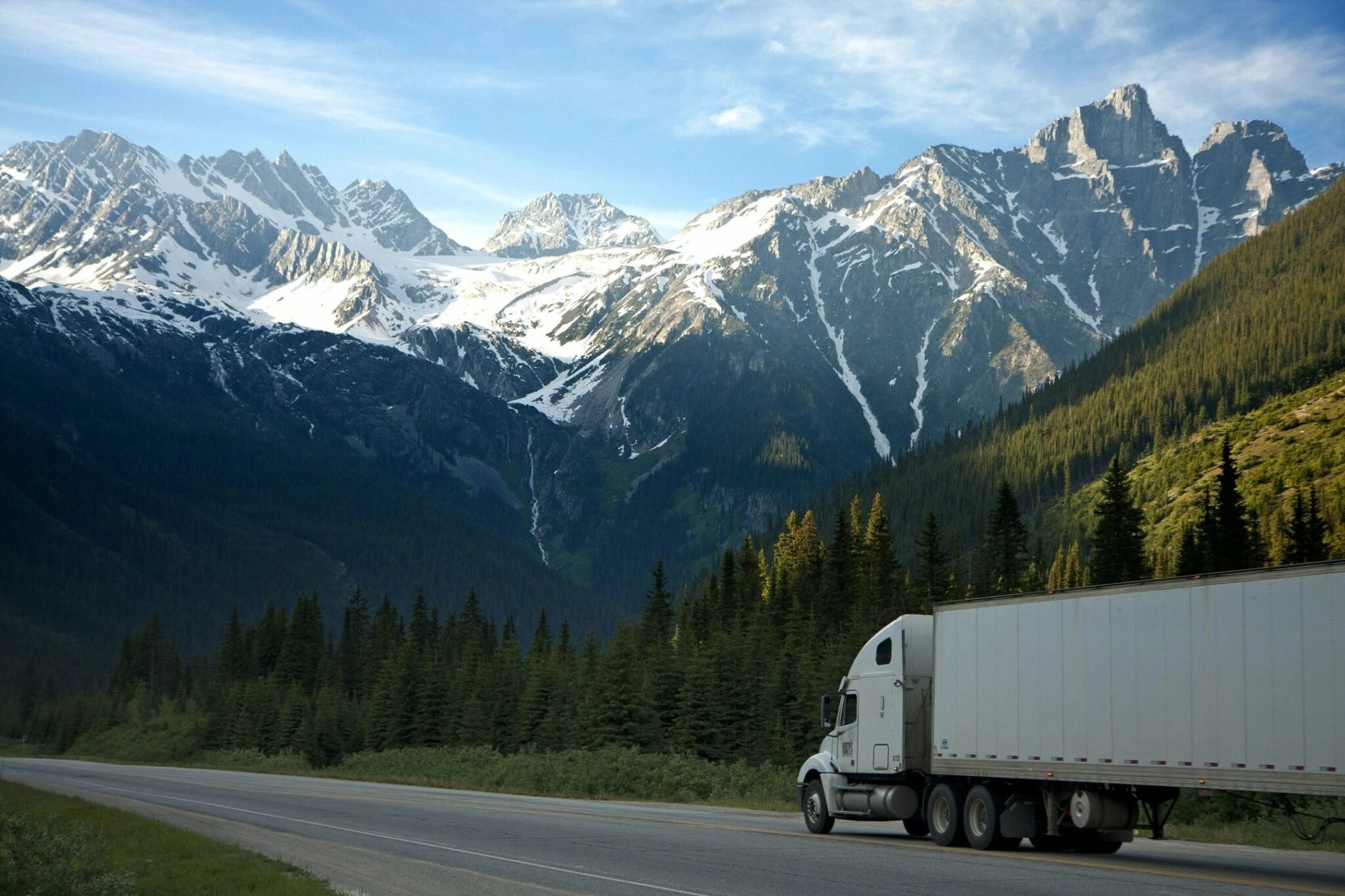 A white truck driving down the road near some mountains.