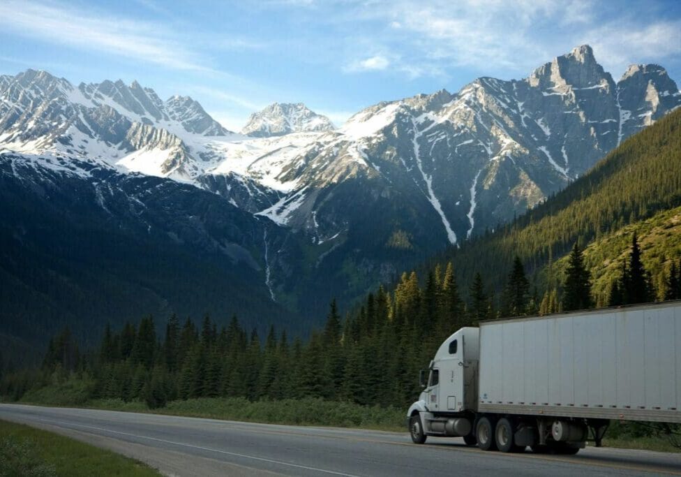 A white truck driving down the road near some mountains.